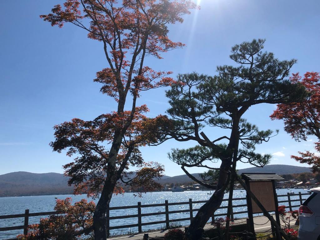two trees next to a fence next to a body of water at Sun Plaza Hotel Fuji Lake Yamanaka in Yamanakako