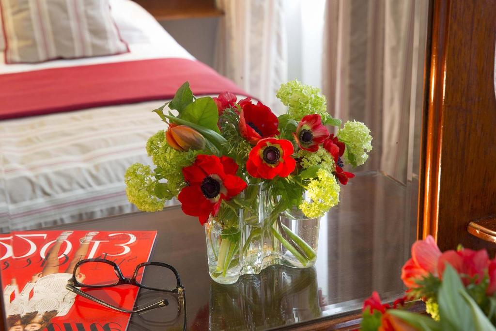 a vase of flowers on a table next to a bed at New Orient Hotel in Paris