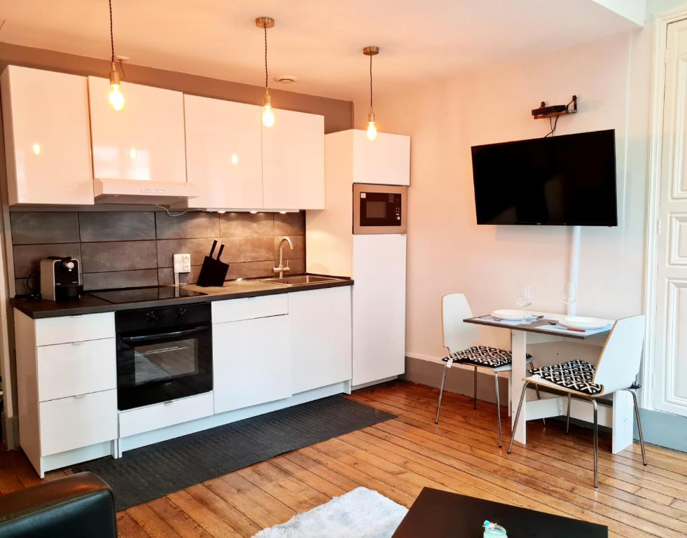 uma cozinha com armários brancos, uma mesa e uma televisão em Le Citadin chic em Dreux