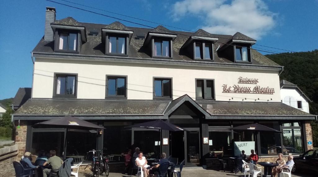 ein großes weißes Gebäude mit Leuten, die draußen sitzen in der Unterkunft Auberge Le Vieux Moulin in Poupehan