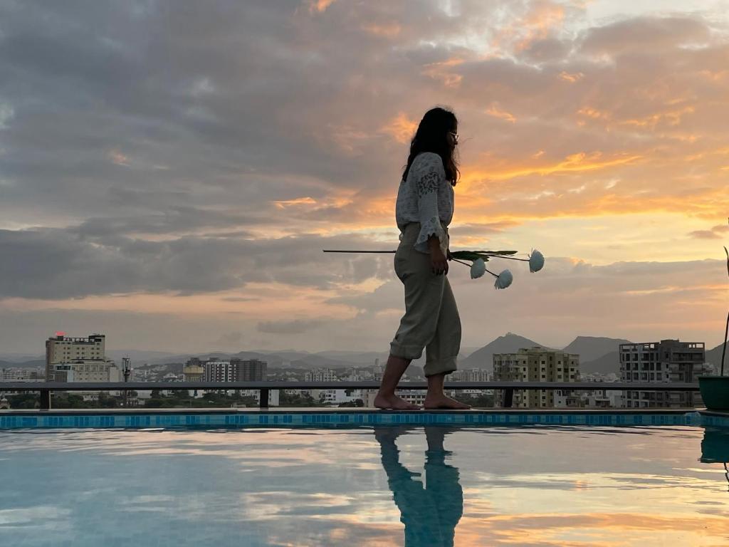 a woman standing on the edge of a pool holding a drone at Clover Inn in Udaipur