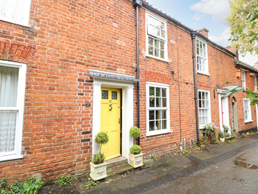 a brick house with a yellow door on a street at Valentine Cottage in Aylsham