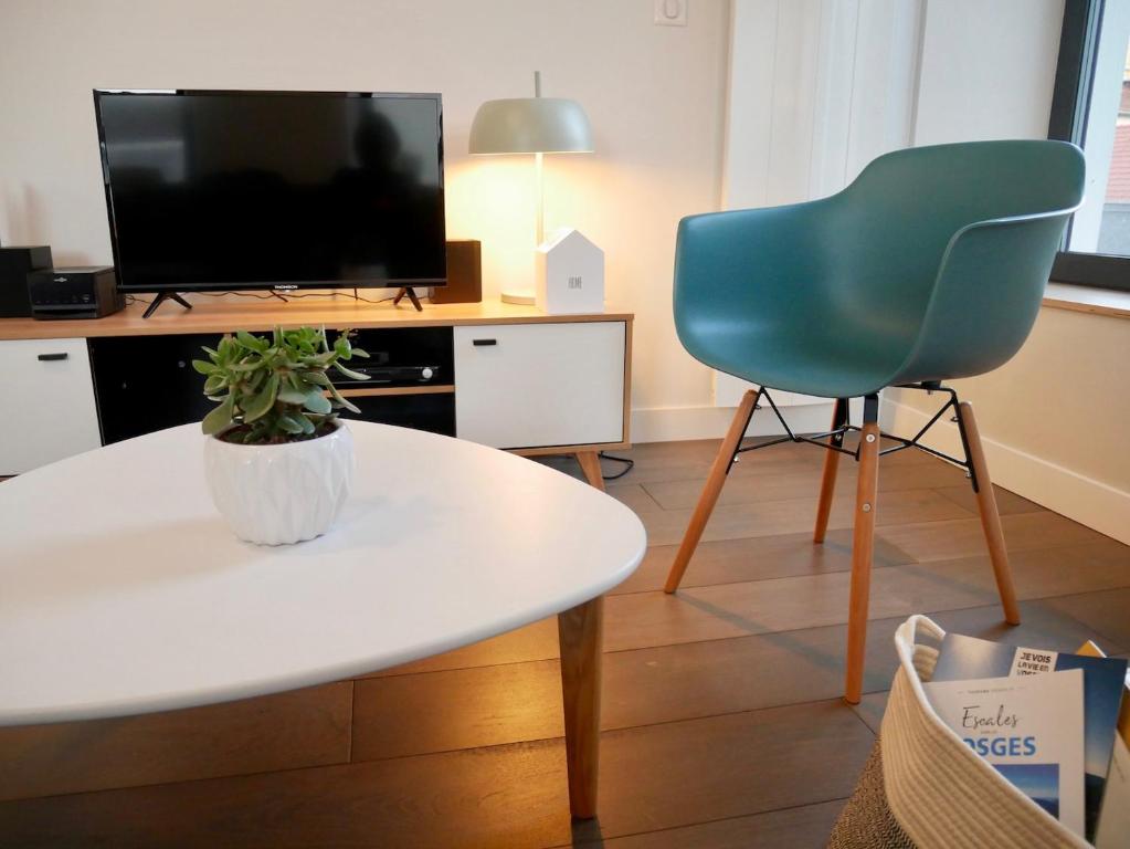 ein Wohnzimmer mit einem Tisch, einem Stuhl und einem TV in der Unterkunft chez Nous in Vittel