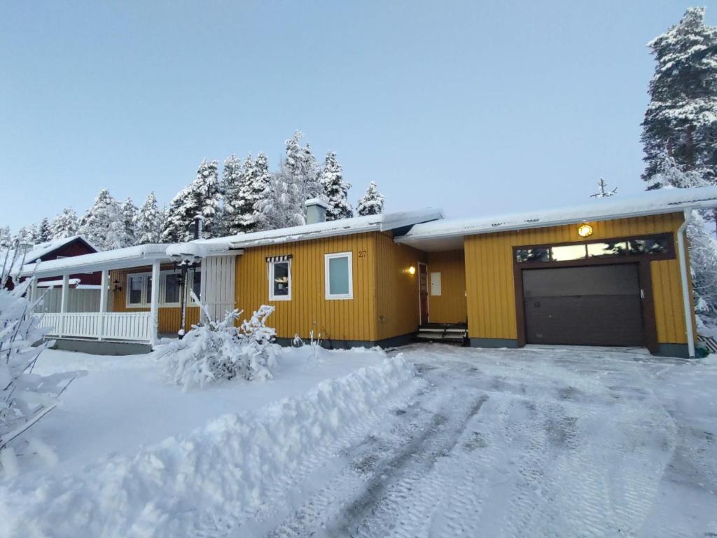 uma casa amarela com uma garagem na neve em Lagomhuset - A peaceful holiday in Swedish Lapland em Vidsel