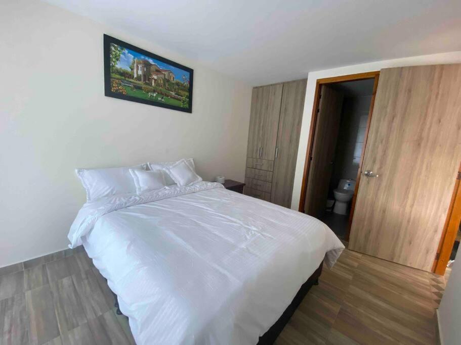 a bedroom with a white bed with a picture on the wall at Hermoso apartamento in Barbosa