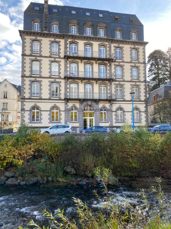 un gran edificio con coches estacionados frente a un río en Grand appartement hyper centre haut standing, en La Bourboule