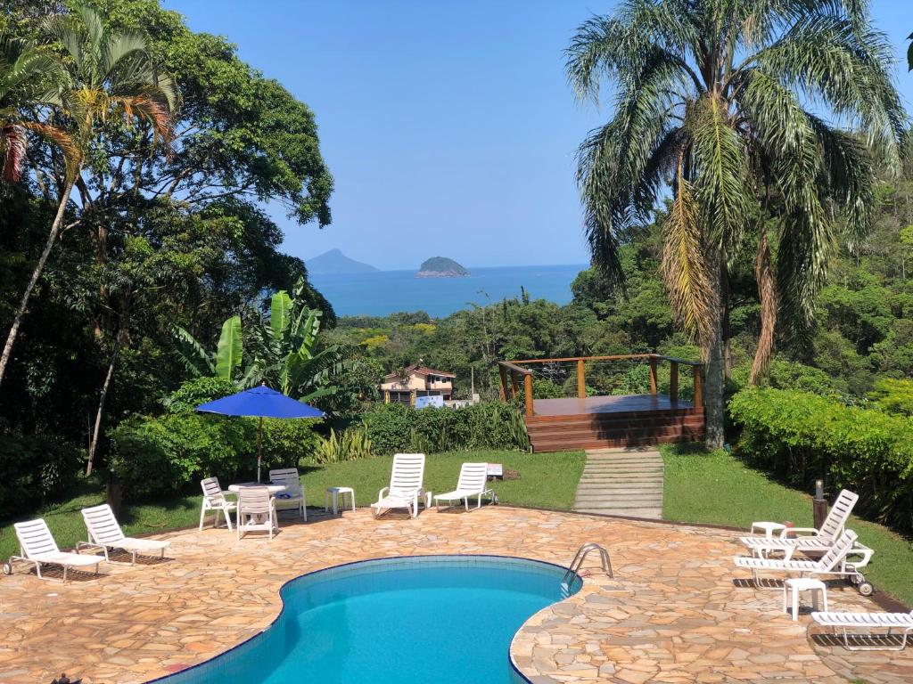 a swimming pool with lounge chairs and an umbrella at Chalé Boiçucanga - Condomínio Village do Mirante in Boicucanga