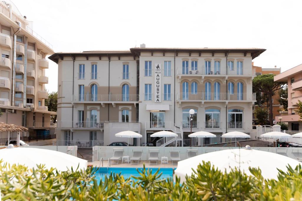 un hotel con sedie e ombrelloni di fronte a un edificio di Hotel Villa Augustea a Rimini