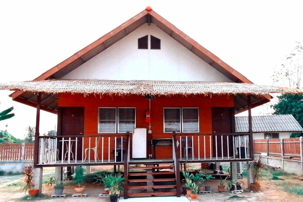 een rood huis met een rieten dak bij บ้านสวนยายชุ่ม/bannsuanyaychum in Lampang