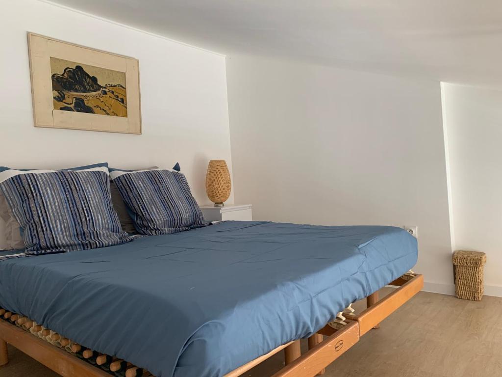 Una cama con sábanas azules y almohadas en un dormitorio en studio mezzanine vue mer terrasse et parking en Sète