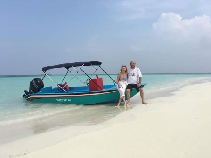 a man and woman sitting on a beach next to a boat at Himandhoo Travel & Stays in Alifu Atoll