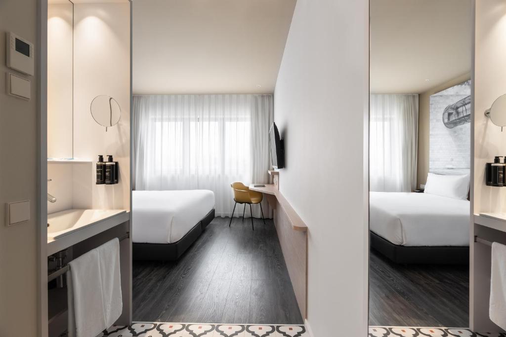A twin room viewed from the entrance, with a compact vanity, two beds, and a desk by the window.