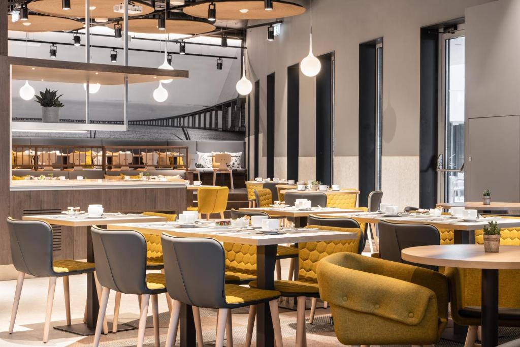 A bright breakfast room with a buffet counter, high chairs, and tables beside tall windows.
