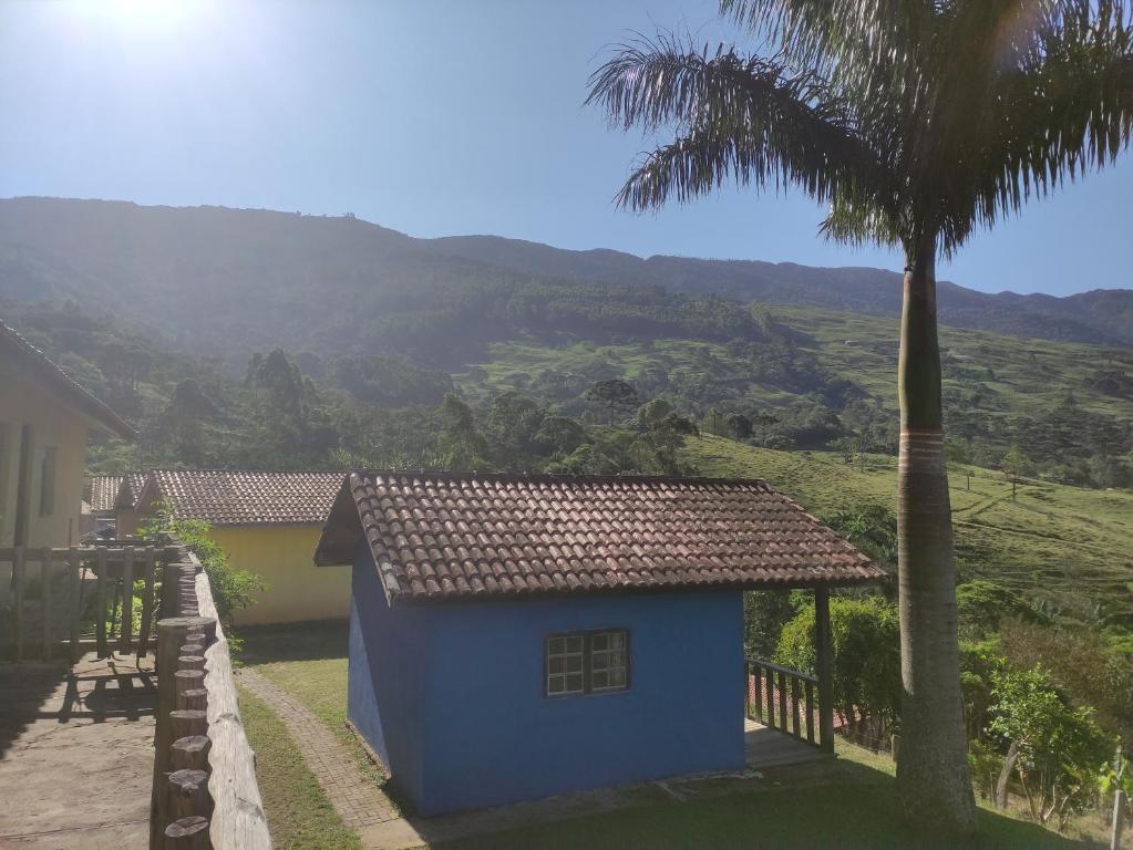 une maison bleue avec un palmier et une montagne dans l'établissement Pousada e restaurante Além das Nuvens, à Guaratinguetá