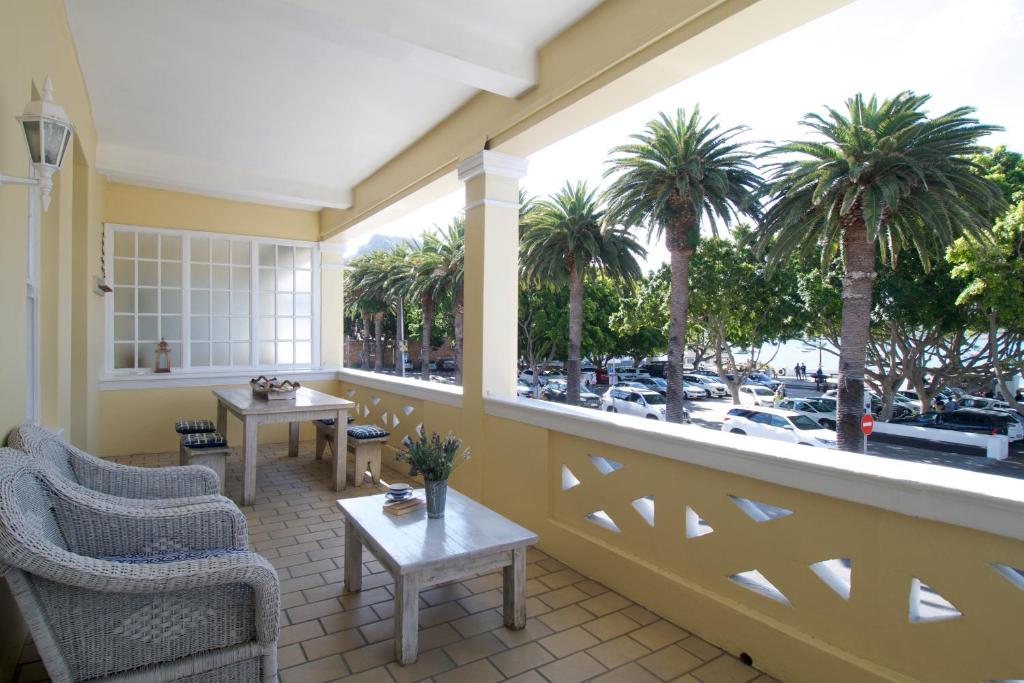 un balcón con sillas, mesas y palmeras en On The Square Luxury Apartment, en Simonʼs Town