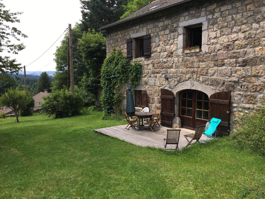 a stone house with a wooden deck in the yard at GITE LES MYOSOTIS in Le Chambon-sur-Lignon