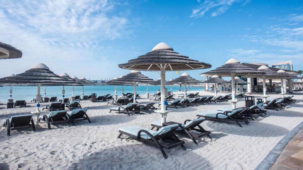 a beach with chairs and umbrellas and the ocean at InterContinental Abu Dhabi by IHG in Abu Dhabi