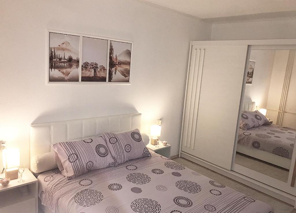 een witte slaapkamer met een bed en een spiegel bij Apartman Dunja in Prijedor