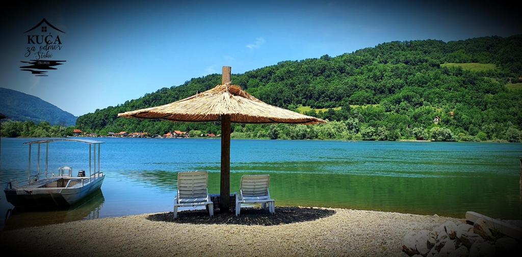 due sedie e un ombrellone e una barca su un lago di Kuća za odmor Stakić - Zvorničko jezero a Zvornik