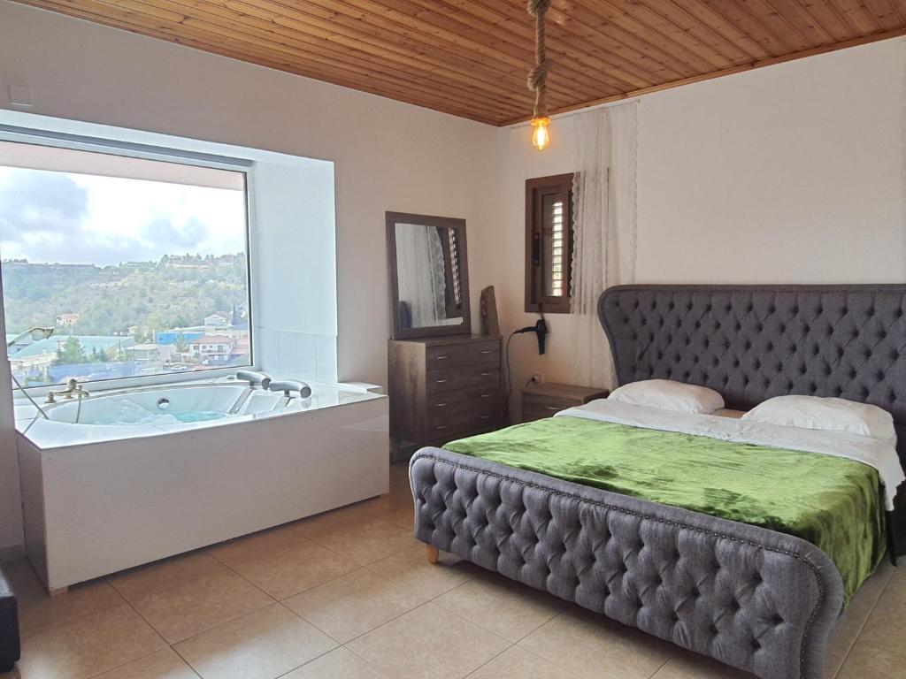 a bedroom with a bed and a tub with a window at Aprosmeno Jacuzzi House 1 in Agros