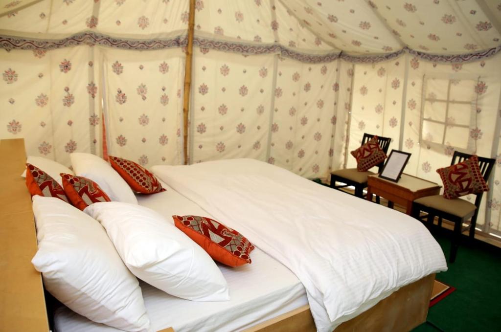 um quarto com uma cama com lençóis brancos e almofadas vermelhas em Kingfisher Desert Camp em Jaisalmer