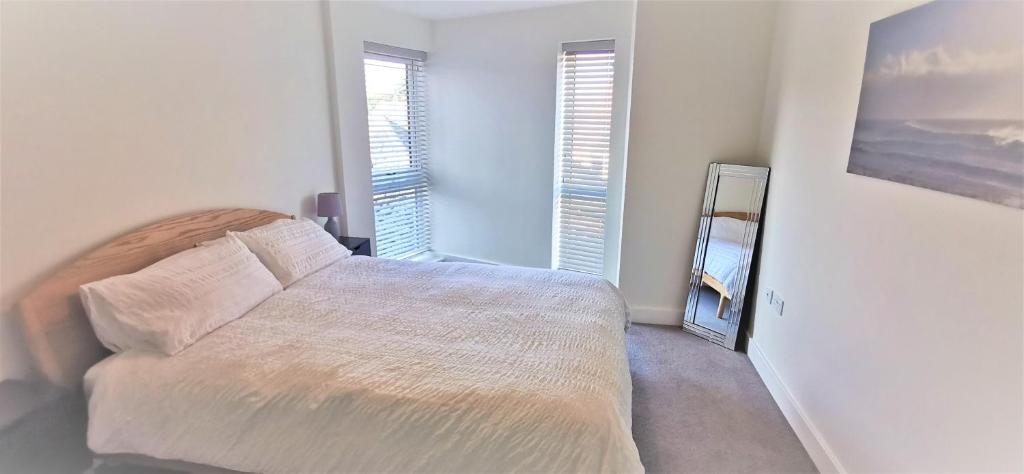 a white bedroom with a bed and two windows at Sea Breeze, gorgeous 2 bed apartment in Exmouth in Exmouth