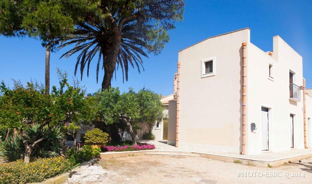 a white building with a palm tree and flowers at Casolare Nelle Saline in Torre Nubia