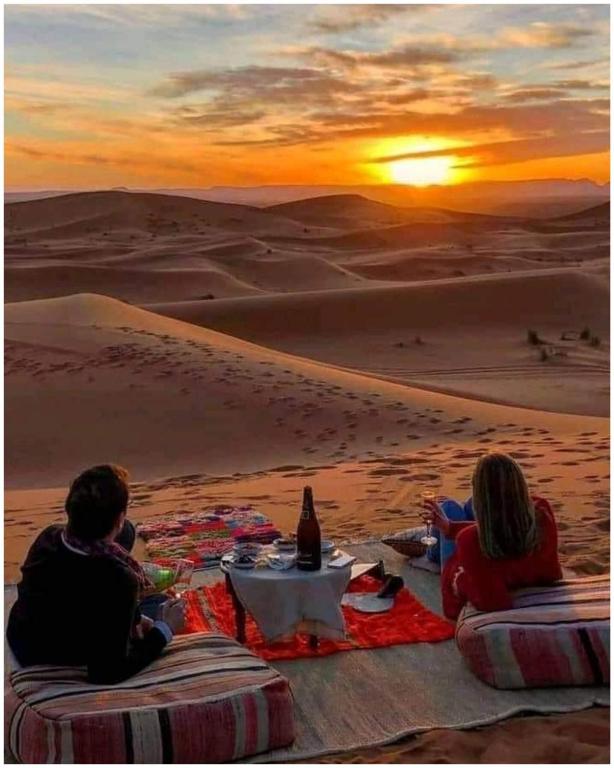 a group of people sitting in the desert watching the sunset at Mhamid Regency Camp in Mhamid