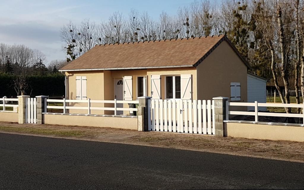ein kleines Haus mit einem weißen Zaun neben einer Straße in der Unterkunft Maison La prairie porte de Chambord in Thoury