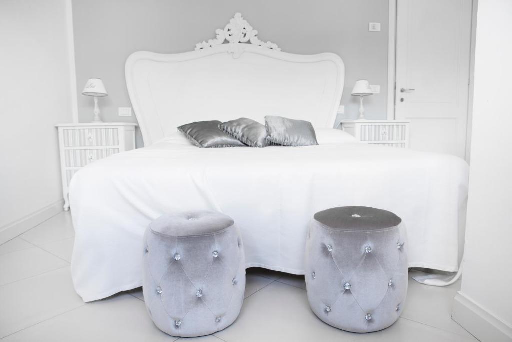 a white bedroom with a white bed and two stools at B&B The Divine in Verbania