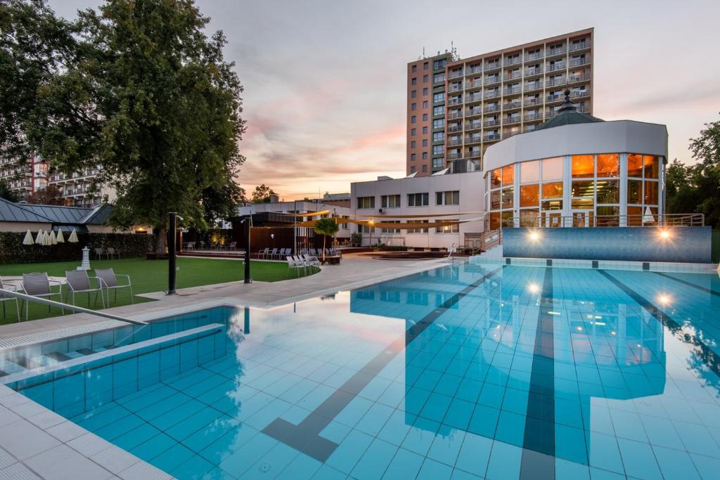 a hotel swimming pool with a building in the background at Hotel Barátság in Hajdúszoboszló