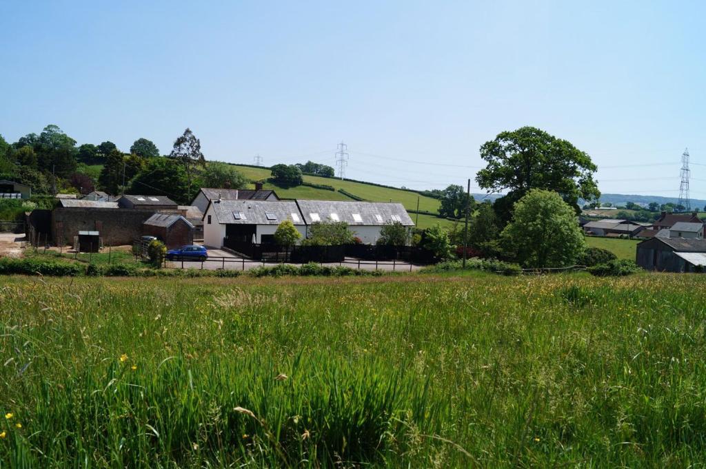 a field of grass with a house in the background at Lower Curscombe Barn - Beautiful 400-year-old threshing barn. Pet-friendly. in Buckerell