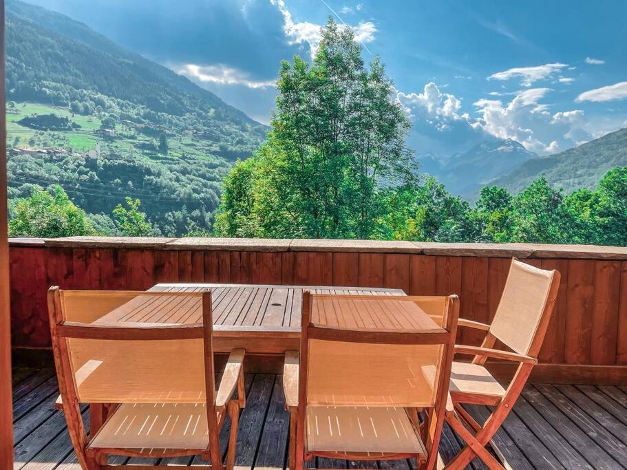 a wooden table and chairs on a deck with mountains at Bel appartement au calme vue vallée in Sainte-Foy-Tarentaise
