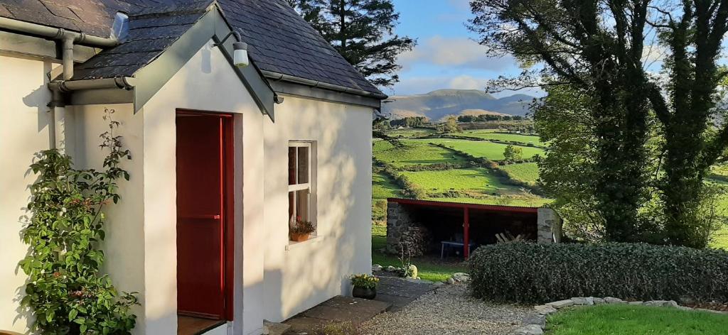 a small white house with a red door and a field at Drumena Cottage in Kilcoo