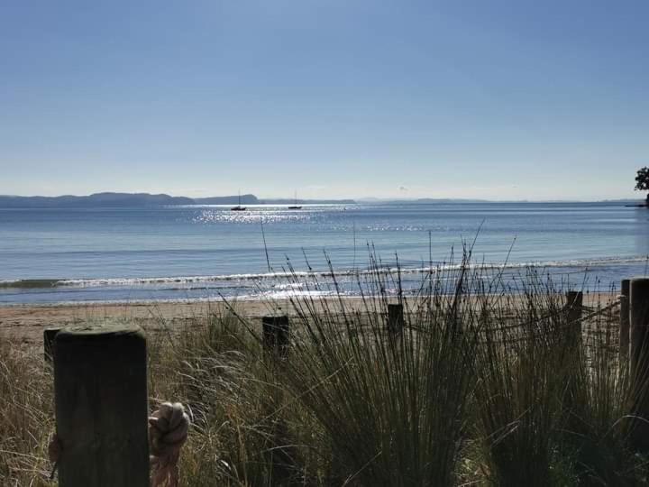 uma vista para uma praia com uma cerca e para o oceano em Stanmore Bay Beach House em Península de Whangaparaoa