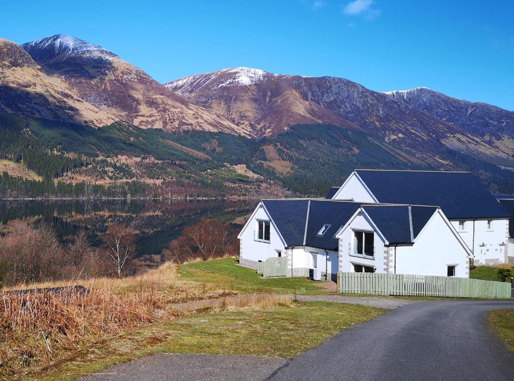 a white house on the side of a road with mountains at Lochside, 1 The Corries in Spean Bridge