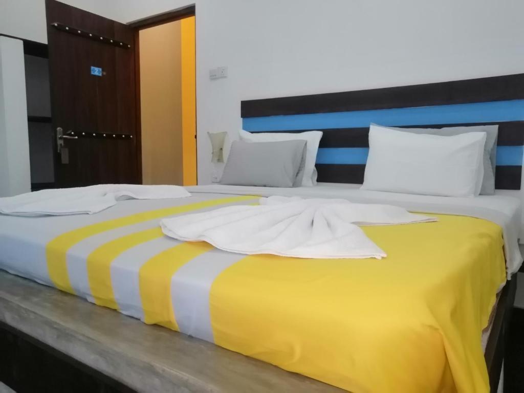 a large bed with a yellow and white blanket on it at Le Petit Hotel & Restaurant in Negombo
