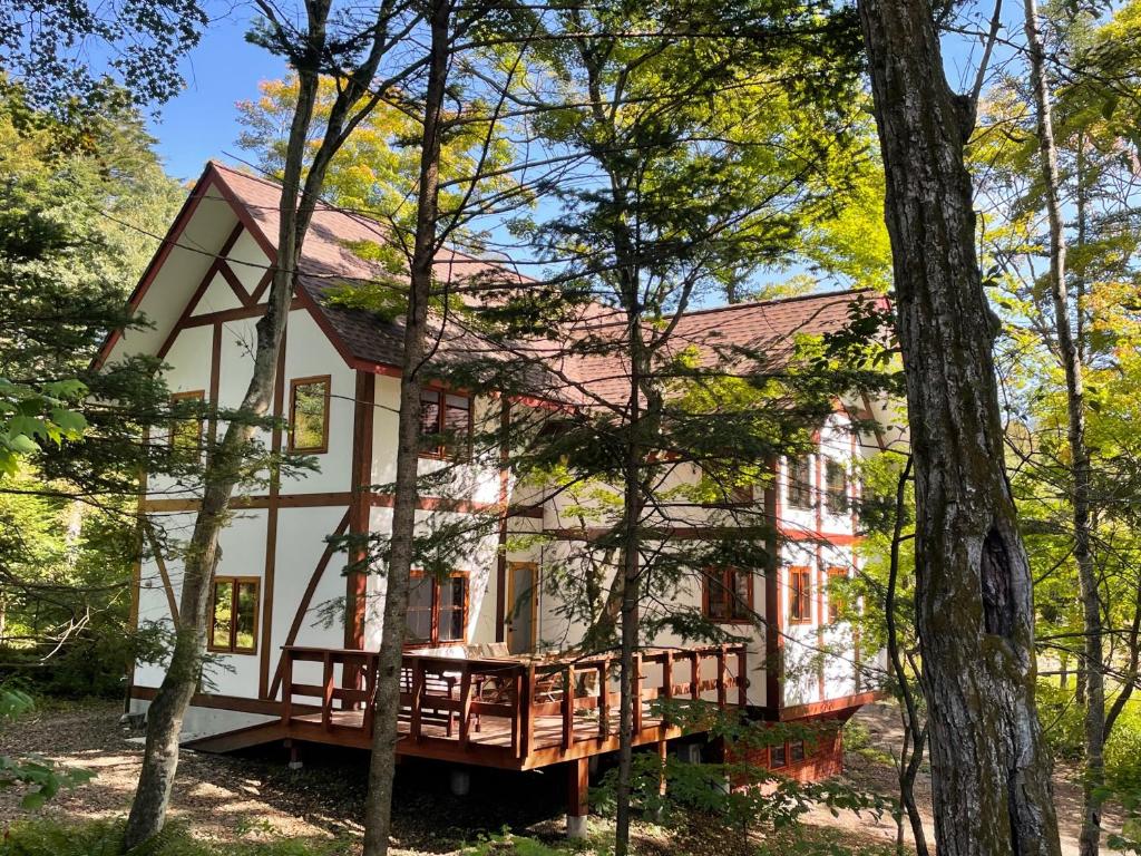 uma grande casa branca com um alpendre na floresta em 軽井沢メイプルチューダーハウス em Karuizawa