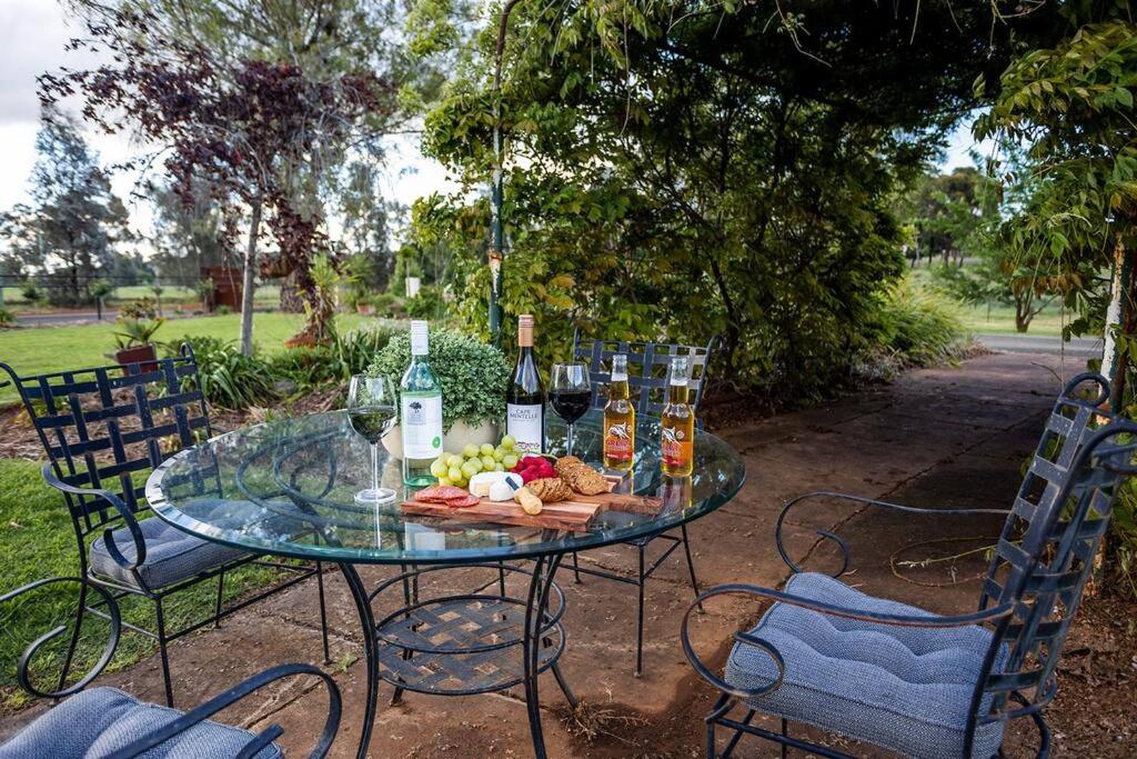 un tavolo di vetro con bottiglie di vino e cibo sopra di EdenValley Private Manicured Gardens with Fire Pit a Parkes