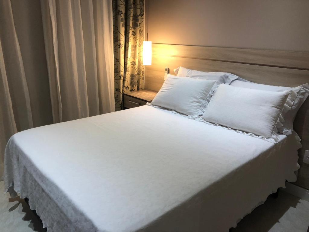1 cama con sábanas blancas y almohadas en una habitación en Flat 5 estrelas-novo e charmoso na Granja Viana, en Cotia