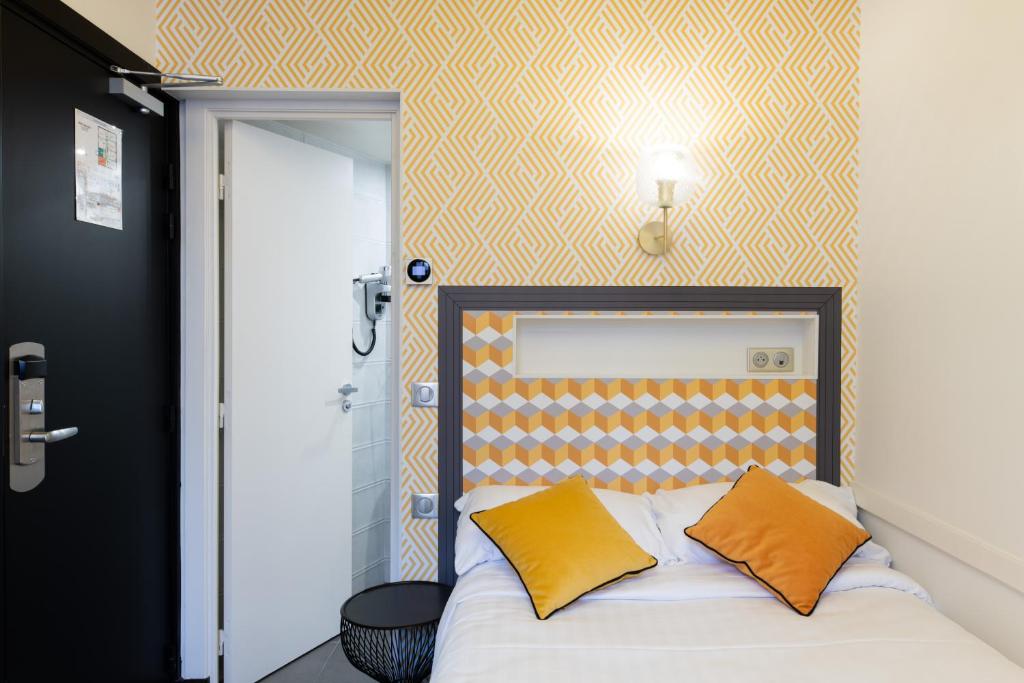 a bed with two orange pillows in a room at Hôtel Gérando in Paris
