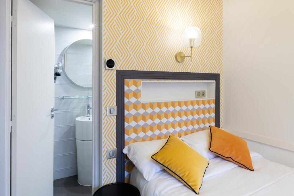 a bedroom with a bed with orange and yellow pillows at Hôtel Gérando in Paris