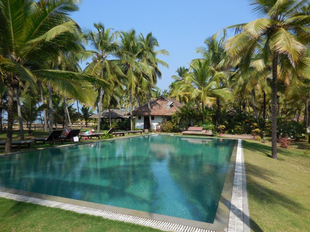 a swimming pool in front of a resort with palm trees at Kanan Beach Resort in Nīleshwar