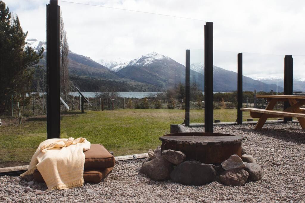 a fire pit with a table and mountains in the background at Cabaña frente al lago Meliquina in Lago Meliquina