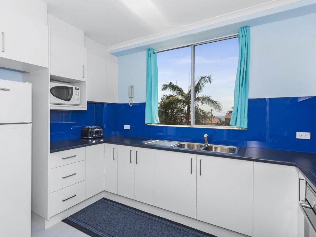 a blue kitchen with white cabinets and a window at Fairleigh Unit 1 in The Entrance