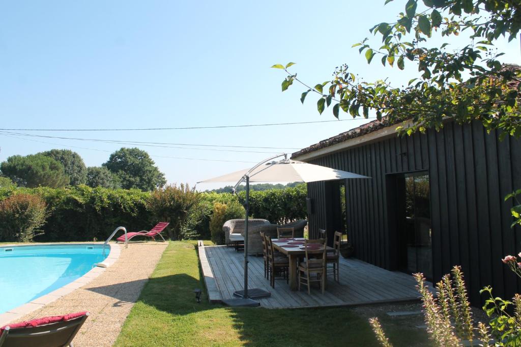 um pátio com uma mesa e um guarda-sol ao lado de uma piscina em La Bastide em Lagrange