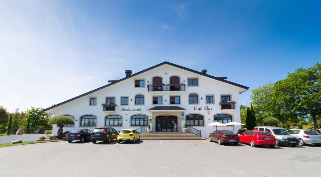 ein großes weißes Gebäude mit Autos auf einem Parkplatz in der Unterkunft Hostal Restaurante O'Cadaval in Frades