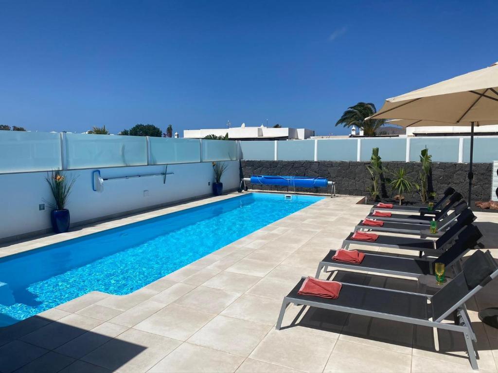 a swimming pool with lounge chairs and an umbrella at Villa Ashdene - luxury modern villa with large heated pool wifi uk tv bar & BBQ in Playa Blanca