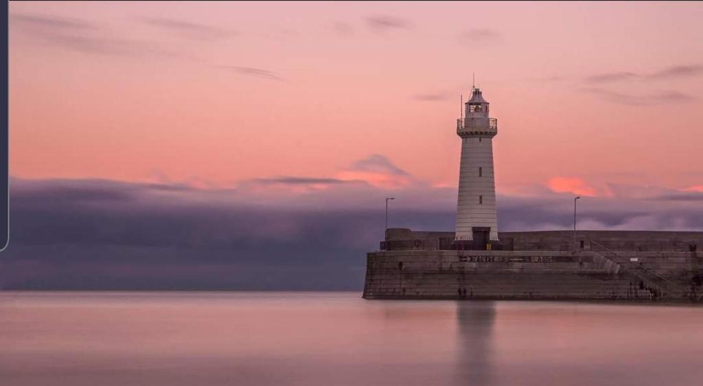 a lighthouse sitting on top of the water at Home from Home 3 bedroom pier front stay in Donaghadee