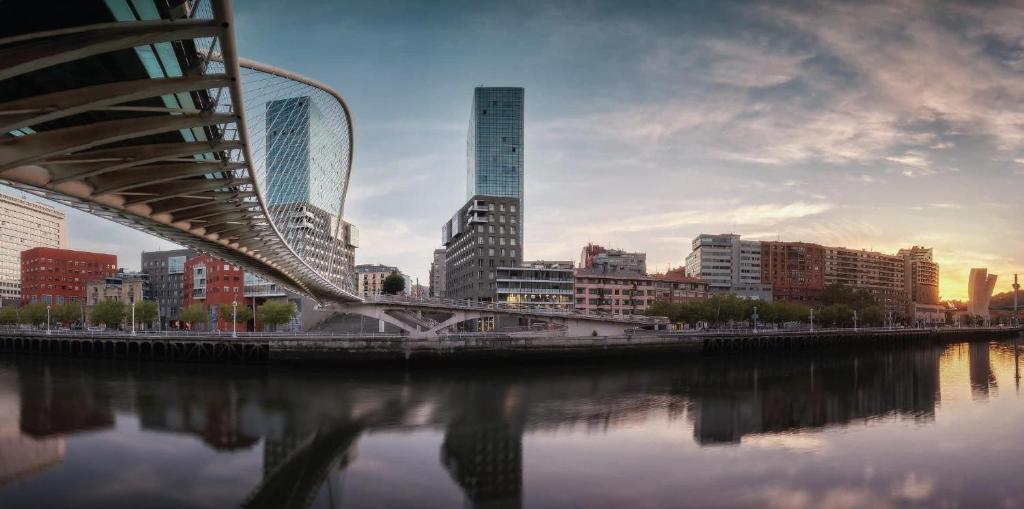 Bilbao City Center by abba Suites في بلباو: جسر فوق نهر في مدينة بها مباني